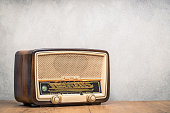 Retro broadcast table radio receiver with green eye light, studio microphone circa 1950 on wooden desk front concrete wall background. Listen music concept. Vintage instagram old style filtered photo