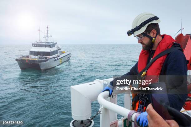 operaio offshore in attesa della nave di trasferimento con turbine eoliche dietro di lui. - life jacket photos foto e immagini stock