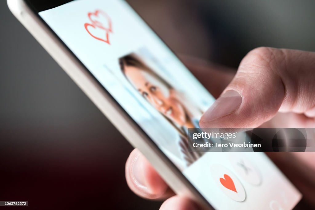 Online dating app in smartphone. Man looking at photo of beautiful woman. Person swiping and liking profiles on relationship site or application. Single guy searching for love partner.