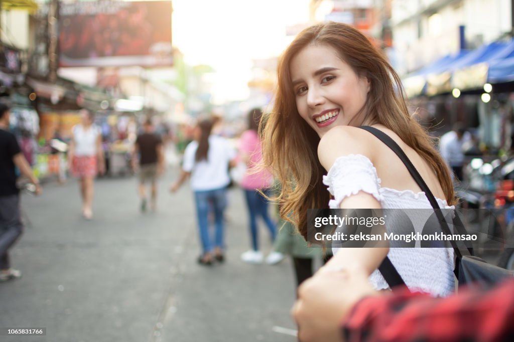 Couple summer vacation travel. Woman walking on romantic honeymoon promenade holidays holding hand of husband following her, view from behind. (focus on woman)