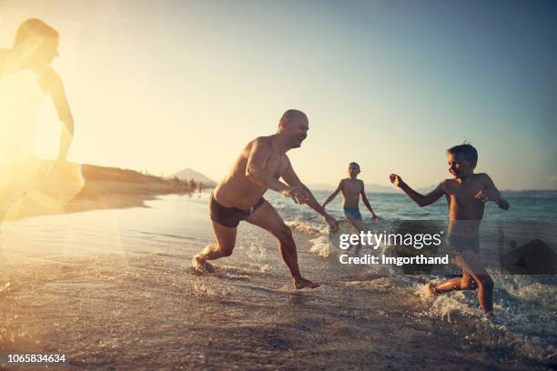 vater und kinder spielen am strand - fangspiel stock-fotos und bilder