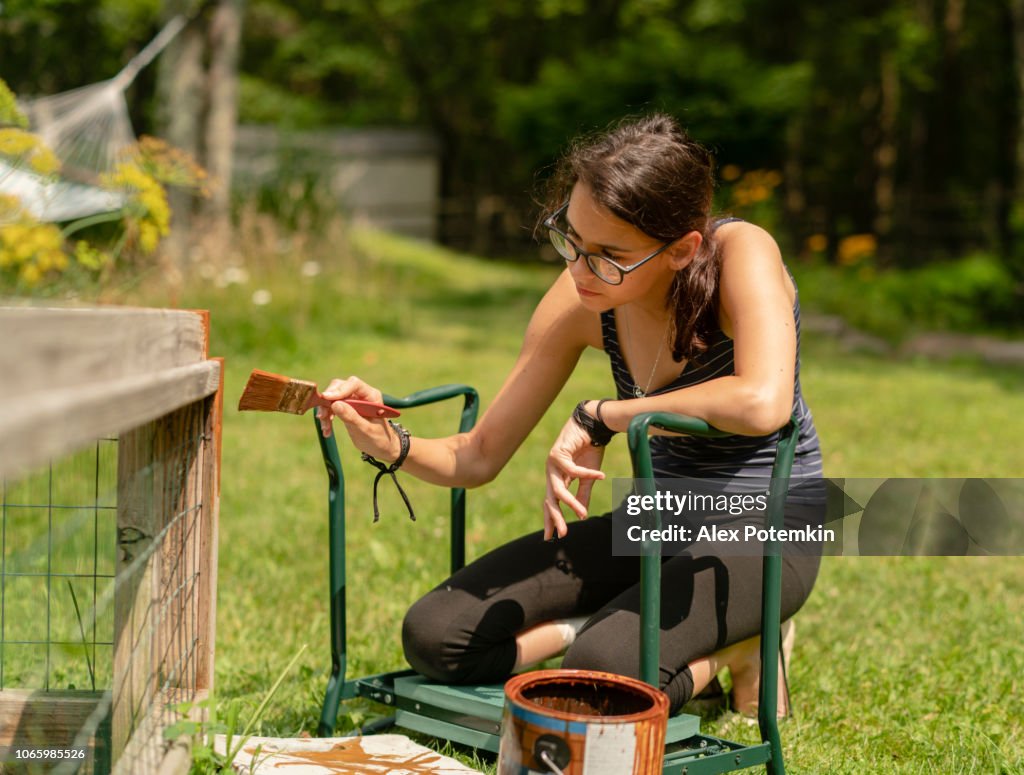 The attractive 15-years-old teenager girl painting the fence at the backyard