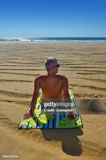 hombre joven sentado en la playa mirando al mar - hombre sentado stock-fotos und bilder