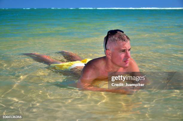 hombre joven disfruta de un baño en una laguna poco profunda disfrutando del sol y la playa - un solo hombre joven stock pictures, royalty-free photos & images