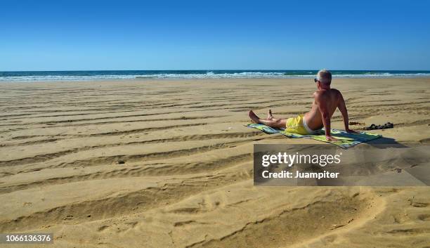 hombre joven sentado en la playa mirando al mar - hombre joven stock pictures, royalty-free photos & images