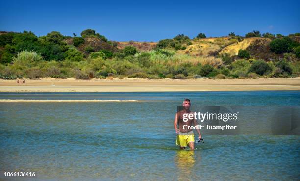 hombre joven solitario cruza andando una laguna a pie disfrutando  del sol y la playa - hombre joven stock pictures, royalty-free photos & images