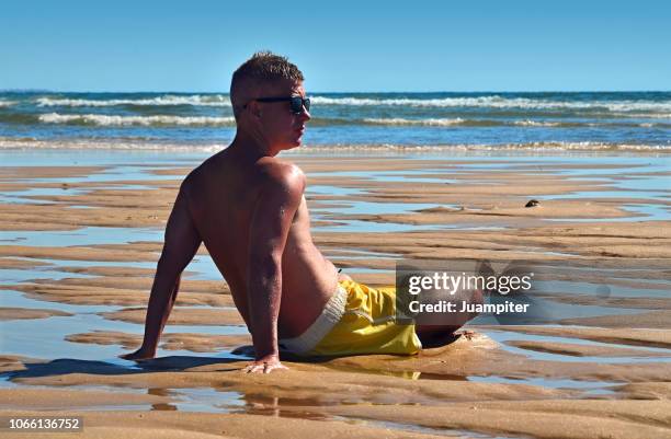 hombre joven sentado en la playa mirando al mar - hombre sentado stockfoto's en -beelden