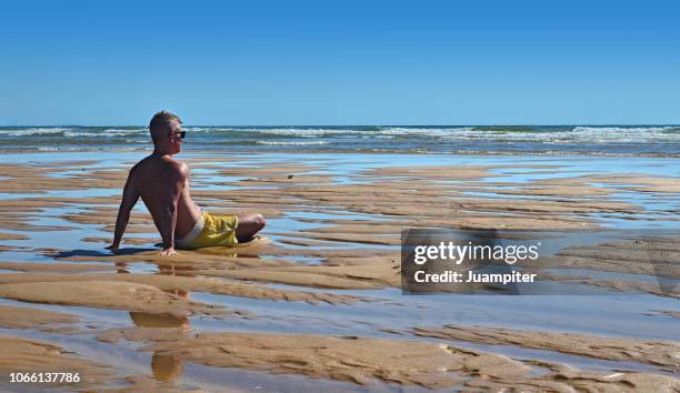 hombre joven sentado en la playa mirando al mar - hombre joven stock pictures, royalty-free photos & images