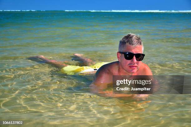 hombre joven disfruta de un baño en una laguna poco profunda disfrutando del sol y la playa - hombre joven stock pictures, royalty-free photos & images