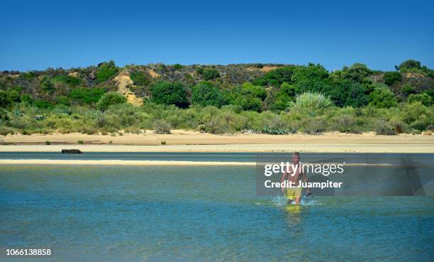 hombre joven solitario cruza andando una laguna a pie disfrutando  del sol y la playa - hombre joven stock pictures, royalty-free photos & images