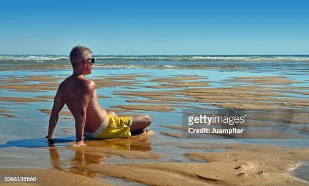 hombre joven sentado en la playa mirando al mar - hombre sentado stockfoto's en -beelden
