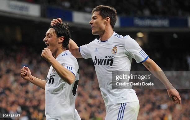 Mesut Ozil of Real Madrid celebrates with Xabi Alonso after scoring Real's second goal during the La Liga match between Real Madrid and Atletico...