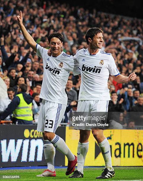 Mesut Ozil of Real Madrid celebrates with Xabi Alonso after scoring Real's second goal during the La Liga match between Real Madrid and Atletico...