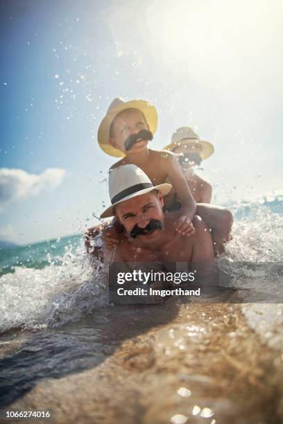 lustige vater und söhne mit schnurrbärten spielen auf hoher see - movember stock-fotos und bilder