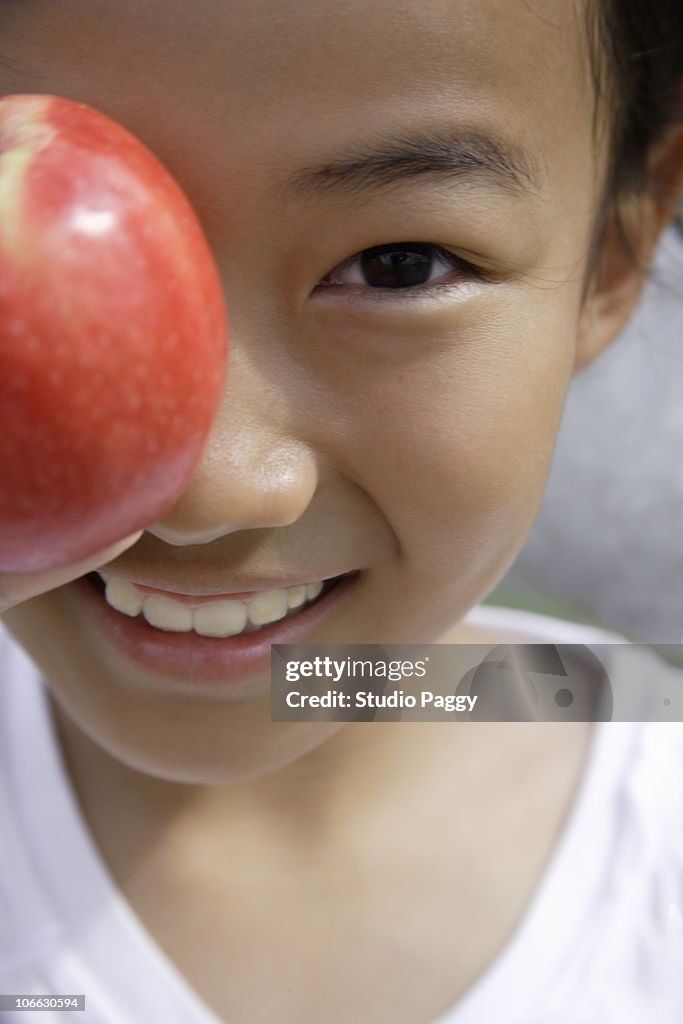 Close-up of a girl holding an apple in front of her eye
