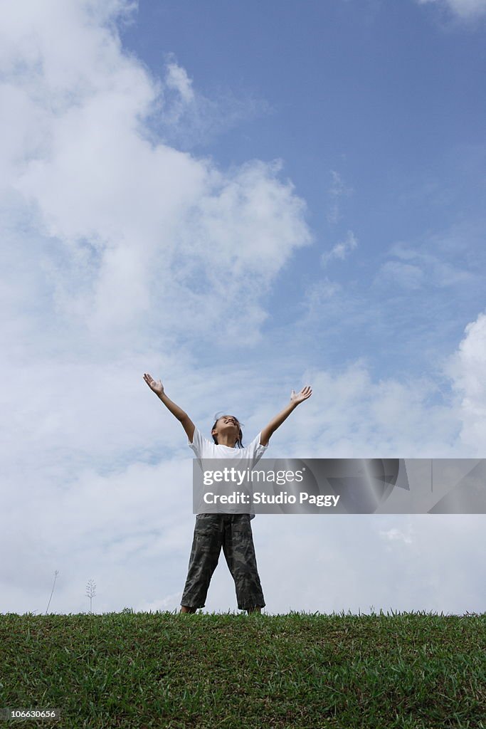 Girl standing with her arms raised looking at sky