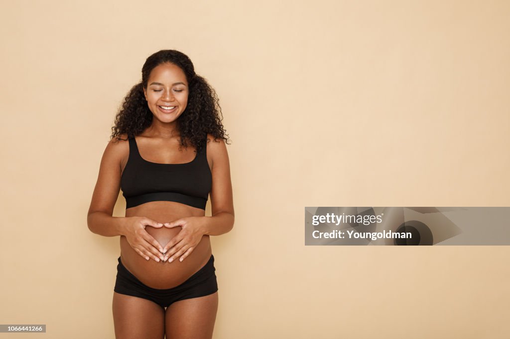 Pregnant woman holding hands on her belly making a heart symbol