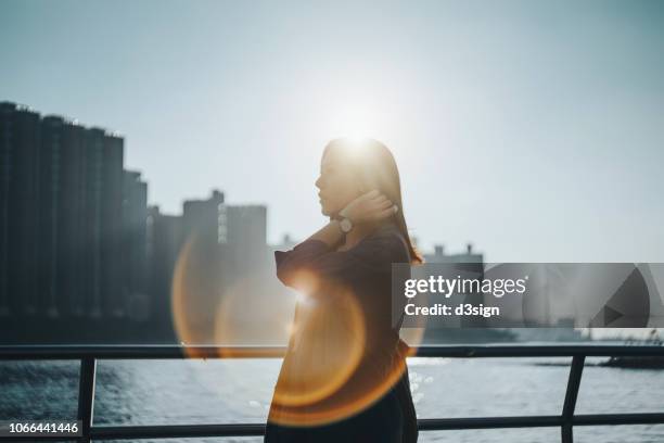 confident young woman standing against urban cityscape and harbour under lens flare with sunlight - hope concept city stock pictures, royalty-free photos & images