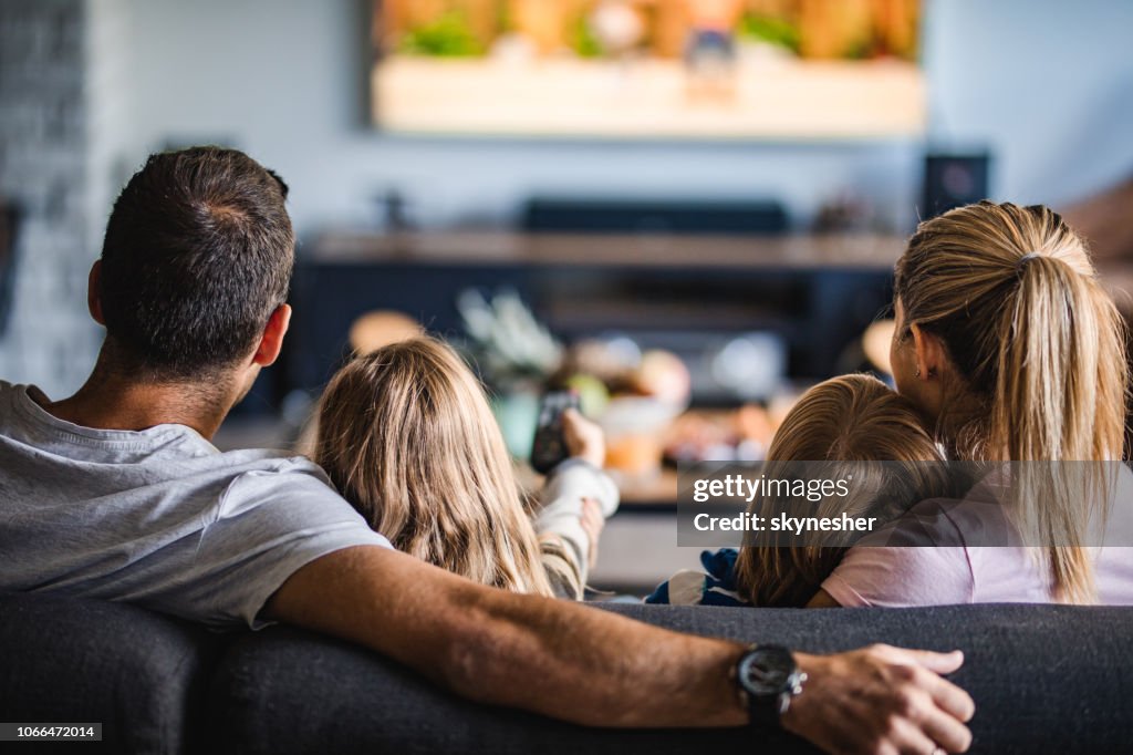 Rear view of a family watching TV on sofa at home.