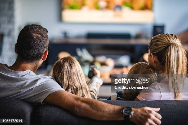 rear view of a family watching tv on sofa at home. - family home imagens e fotografias de stock