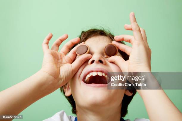 young boy laughing and holding chocolate sweets in front of his eyes - chris chocola stockfoto's en -beelden