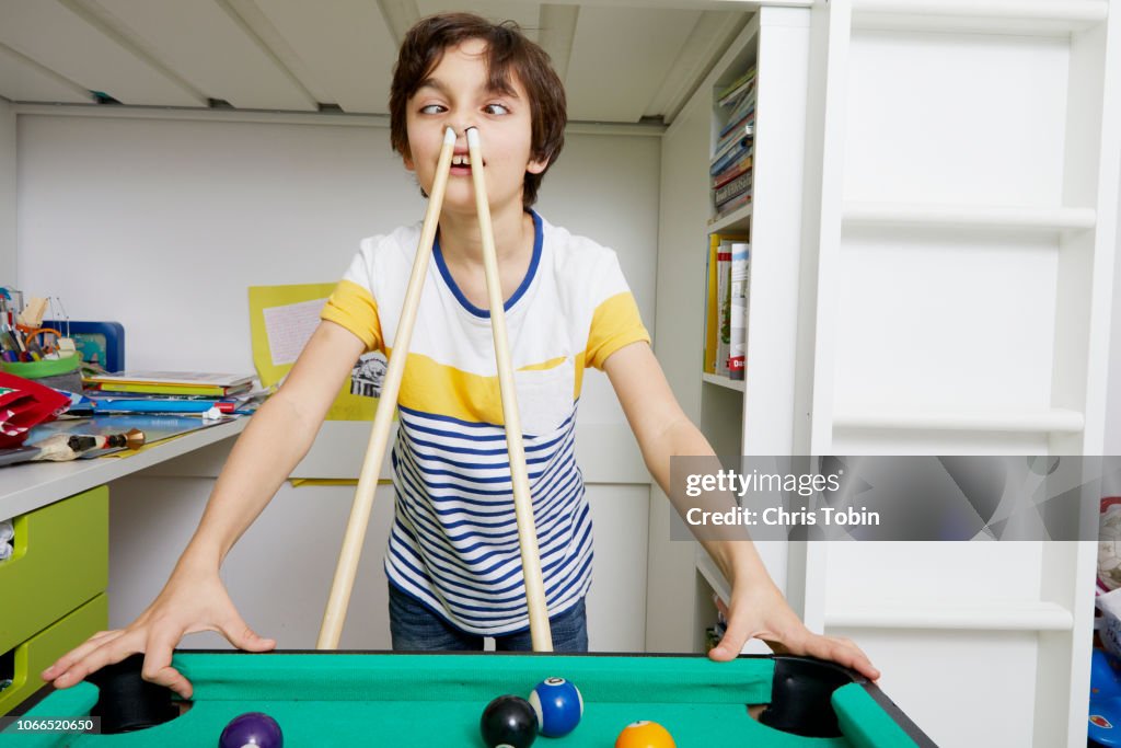 Young boy making faces with billiard cue in his nose