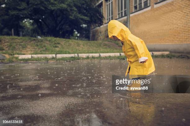 adorable petit garçon jouant au jour de pluie - se protéger de la pluie photos et images de collection