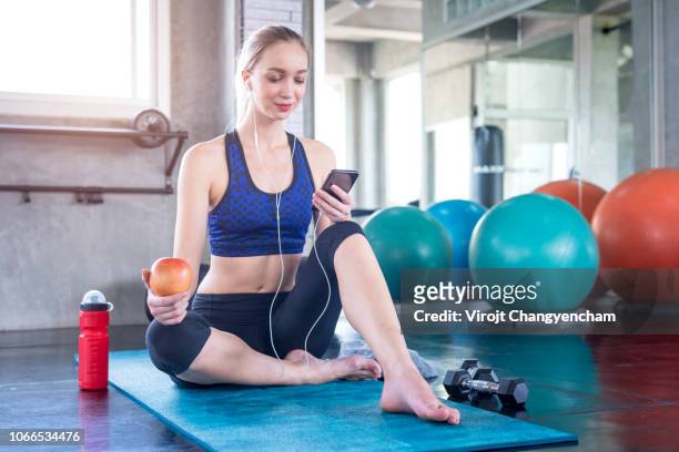 young woman use smartphone and holding red apple after workout in the gym - adult female eating an apple stock pictures, royalty-free photos & images