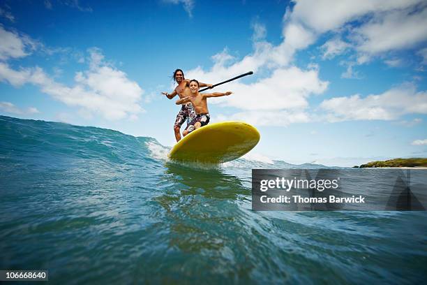 father and son riding wave on stand up paddleboard - remar con pala fotografías e imágenes de stock