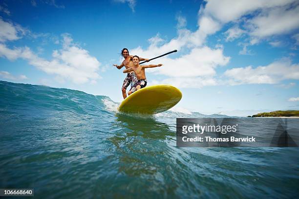 father and son riding wave on stand up paddleboard - isole hawaii foto e immagini stock