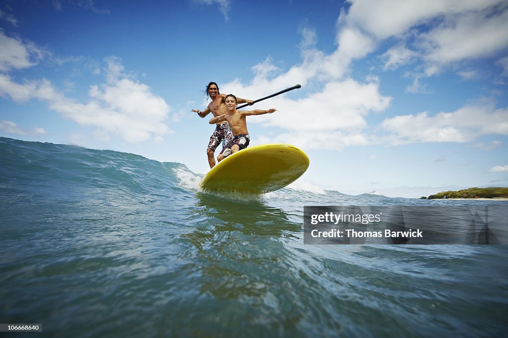 Father and son riding wave on stand up paddleboard