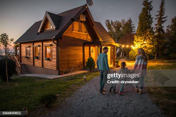 achteraanzicht van gelukkige familie hand in hand en wandelen door hun chalet in de avond. - happy family home outdoors stockfoto's en -beelden