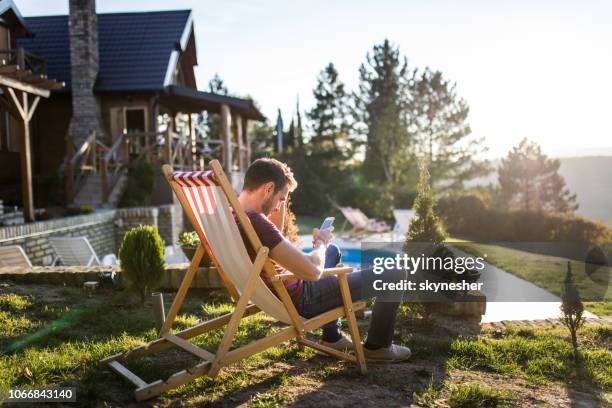 ontspannen man met behulp van slimme telefoon in ligstoel op de achtertuin. - backyard deck stockfoto's en -beelden