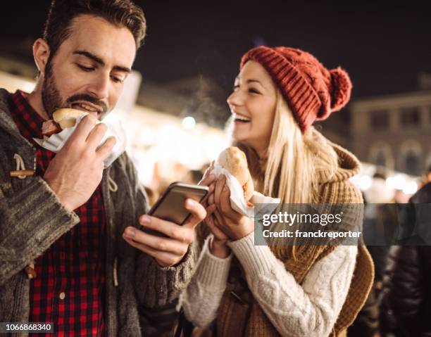 eating street food at the christmas markets in italy - sausage sandwich stock pictures, royalty-free photos & images