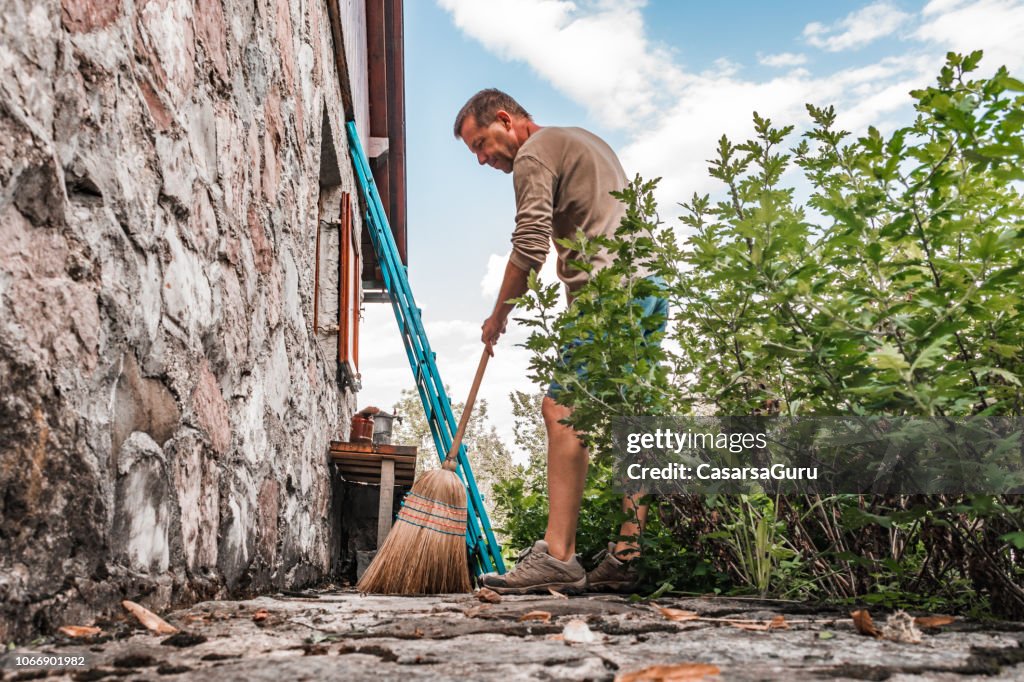 Adult Man Sweeping Front Yard in Rural Scene