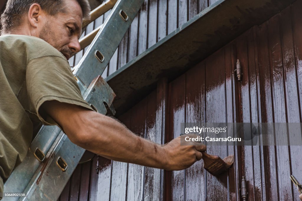 Adult Man Painting an Old House With Protective Paint