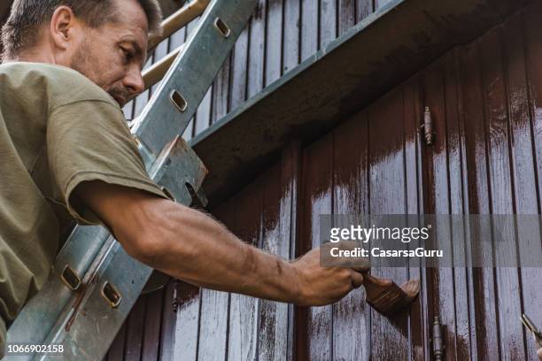 adult man painting an old house with protective paint - painting house exterior stock pictures, royalty-free photos & images