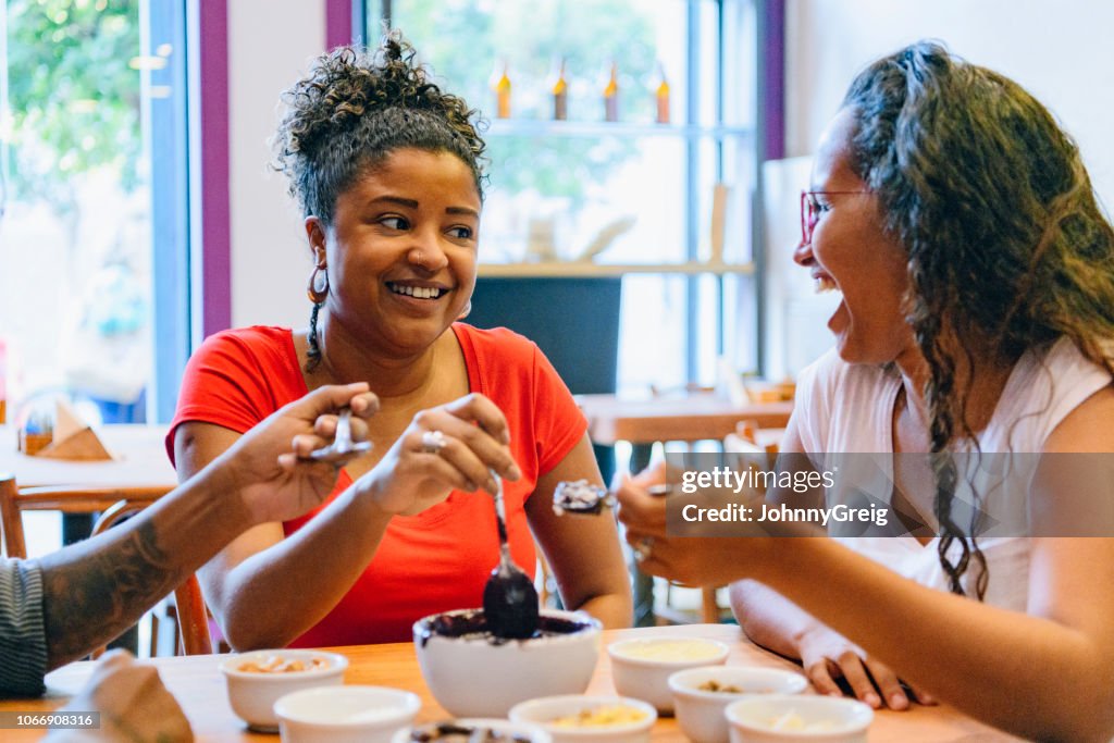 Brazilian friends sharing açai bowl using spoons and smiling