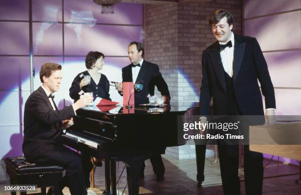 Comic actors Hugh Laurie, Janine Duvitski, Robert Daws and Stephen Fry standing around a piano in a sketch from the BBC television series 'A Bit of...