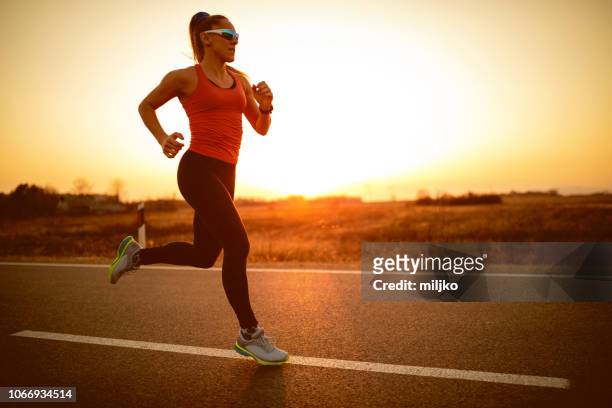 mujer deportista que corre en la carretera al atardecer - carrera de carretera fotografías e imágenes de stock