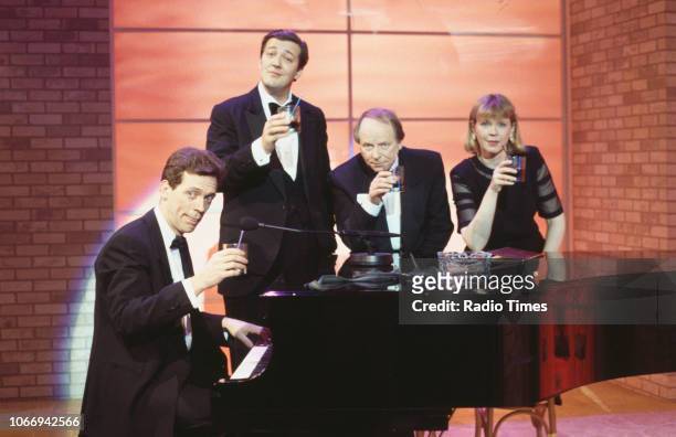Comic actors Hugh Laurie, Stephen Fry, John Bird and Jane Booker standing around a piano in a sketch from the BBC television series 'A Bit of Fry and...