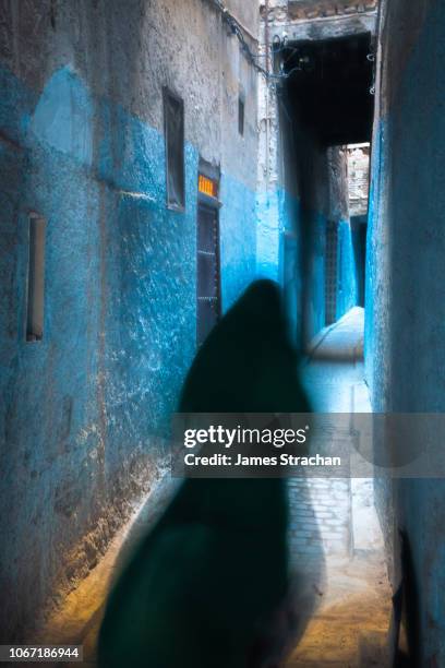 mysterious blurred female figure, her traditional black dress flowing, disappears down an alleyway painted blue in the old city (medina) of fez, unesco world heritage site, morocco - refugee silhouette stock pictures, royalty-free photos & images