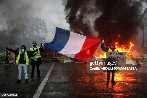 Protesters hold a French flag near a burning barricade during a protest of Yellow vests against rising oil prices and living costs, on December 1,...