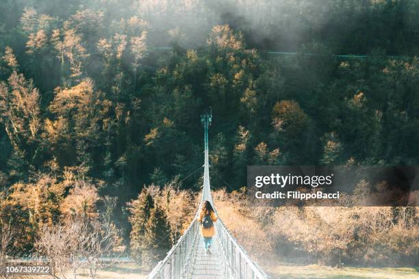 junge frau mit einer gelben jacke auf einer hängebrücke - hängebrücke stock-fotos und bilder