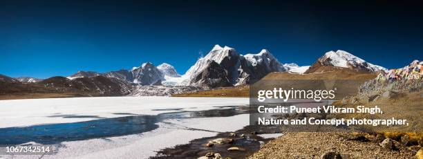 panoramic view of mount kangchengyao which lies in the dongkhya range of mountains as seen from frozen gurudongmar lake in thangu, north sikkim, india. - kangchenjunga stock pictures, royalty-free photos & images