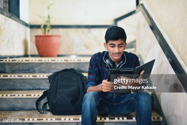 teenager boy using digital tablet while sitting on stairway - indian college students imagens e fotografias de stock