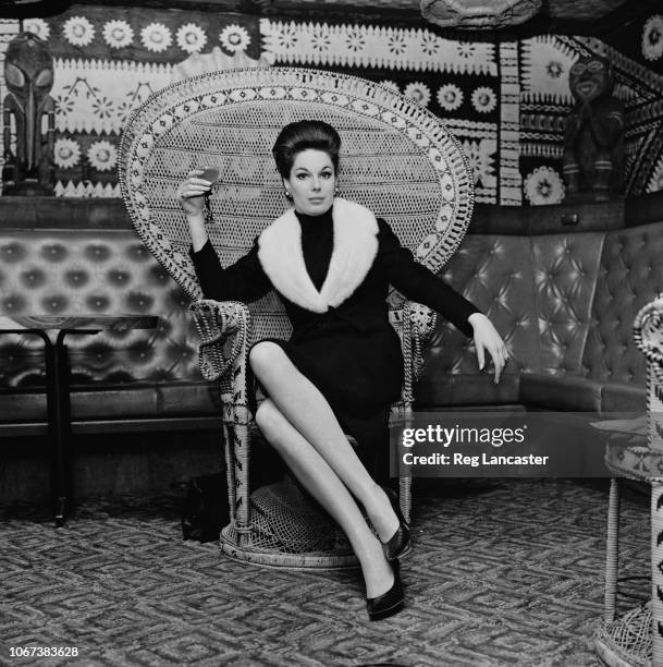 English actress Tracy Reed hold a glass of wine while sitting on a peacock chair, UK, 26th January 1965.
