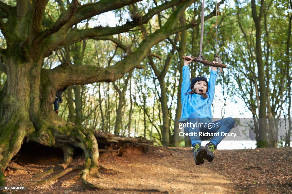 Young girl swinging on a rope swing in woodland