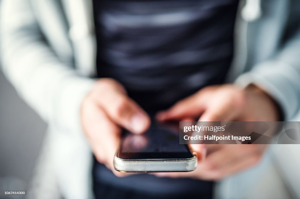 A close-up of unrecognizable young sporty man with smartphone standing in the city.