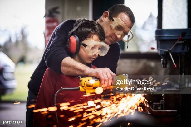 father and son using grinder together in a workshop - kids instruments stock-fotos und bilder